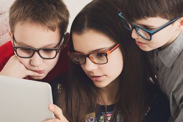 Drei kurzsichtige Kinder schauen auf ein Tablet