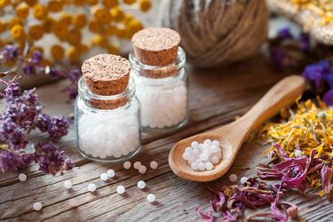 Homöopathische Zutaten (Pflanzen) und Globuli auf einem Holzlöffel