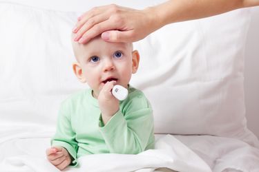 Mutter legt einem Kind das aufrecht im Bett sitzt die Hand auf die Stirn