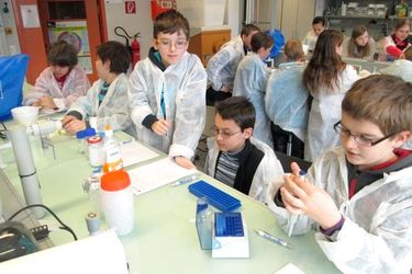 Viele Kinder um einen Tisch mit weißen Laboranzügen
